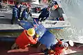 Trois personnes d'un navire de récupération transmettent une pièce métallique de couleur bleue récupérée du fleuve à deux autres personnes dans un autre navire.