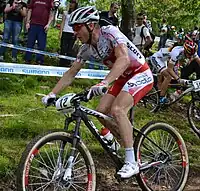 Homme descendant une pente à VTT, portant une tenue rouge et blanche.