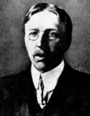 photo noir et blanc, tenue classique avec col rabaissé et cravate, moustache, lunettes