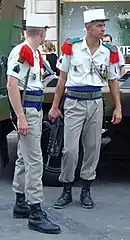 Soldats de la Légion étrangère en uniforme de parade. Épaulettes rouges à parement vert, ceinture bleue et képi blanc distinctif.