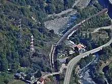 Vue aérienne d’une voie de chemin de fer en courbe, proche d’une route, en fond de vallée.