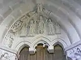 Photographie en couleurs d'une porte surmontée d'un tympan dont seule une partie est sculptée, le reste demeurant brut.