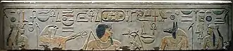 Pierre en grès clair avec des images gravées et peintes montrant deux femmes, un dieu à tête de faucon, un homme aux cheveux noirs avec une longue barbiche, un dieu à tête de chacal et des hiéroglyphes égyptiens inscrits au-dessus.