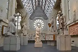  Photographie montrant plusieurs sculptures et statues dans une ancienne église ; toiture en verre et rosace.