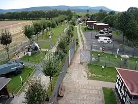 Vue élevée d'une série de cabanes et de véhicules exposés en plein air de chaque côté d'une route de patrouille bétonnée.