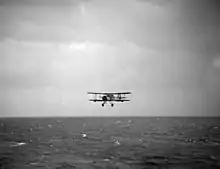 Photo en noir et blanc d'un avion biplan volant au-dessus de l'océan.