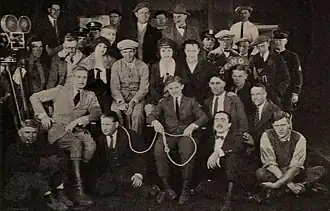 Photographie en noir et blanc de l'équipe du film rassemblée pour l'occasion, avec une caméra montée sur un trépied sur le côté gauche