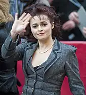 Une femme brune d'une quarantaine d'années, aux cheveux longs et attachés, faisant un signe de sa main droite au photographe.
