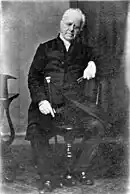 Photographie ancienne en noir et blanc d'un homme blanc âgé assis sur une chaise.