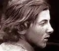 Photographie en noir et blanc d'un jeune homme aux cheveux longs, de profil.