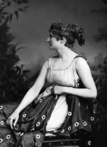 Photo noir et blanc d'une femme en costume, assise et de profil.