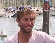 Portrait, souriant, barbu, lunettes de soleil sur ses cheveux en bataille, collés par le sel.