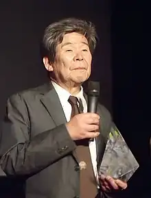Photographie d'un homme âgé en costume avec un micro dans la main.
