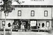 Une photographie ancienne d'un bâtiment portant les inscriptions « Canada », « J. M. Hill » et « U.S.A. ».