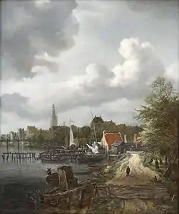Chemin longeant une rivière avec barques amarrées, pont et bâtiments qui se devinent en arrière-plan.