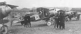 Photo noir et blanc d'avions biplans stationnés devant des hangars avec des groupes d'hommes discutant entre eux devant les appareils
