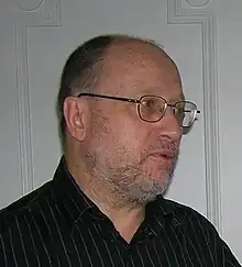 Photographie de profil d'un homme aux cheveux dégarnis, à la barbe courte et portant des lunettes.