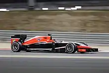 Photo de profil droit d'une monoplace rouge aux flancs noirs, sur un circuit, en nocturne