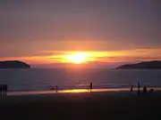 Photographie d'un coucher de soleil sur une place. De part et d'autre de l’horizon se trouvent deux îles.