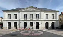 Photographie d'un bâtiment d'un étage sur rez-de-chaussée à sept hautes arcades fermées par des grilles en fer. La partie centrale, surmontée d'un fronton triangulaire, est en légère avancée.