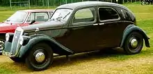 Photo d'une voiture de type berline et de couleur noire stationnée dans l'herbe à côté d'un autre véhicule.