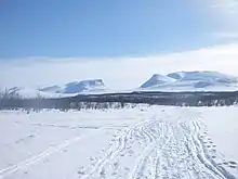 collines enneigées et ensoleillées, à l'horizon une trouée dans le relief forme une porte, quelques traces de ski.