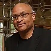 Photographie d’un homme avec des lunettes regardant la caméra en souriant.