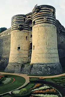 Photographie du château : deux tours et des jardins dans les douves au premier plan.