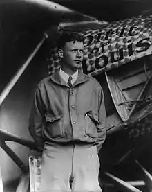 Photographie en noir et blanc d'un homme en blouson d'aviateur se tenant debout devant son avion, le Spirit of Saint Louis.