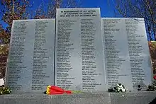 Photo d'un mémorial comportant trois parties en pierres grises. Une partie du milieu et deux parties sur les côtés, qui sont légèrement moins hautes. Sur l'ensemble se trouve des inscriptions écrites en noires.