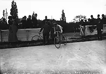 Photographie en noir et blanc montrant un cycliste en course, entrant sur la piste d'un vélodrome.