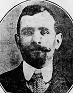 Portrait en noir et blanc de Luigi Galleani en costume, faisant face à l'appareil photo, avec une barbiche et une moustache bouclée à l'extrémité.