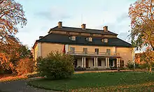 On voit la façade principale du manoir sous un soleil rasant d’automne.