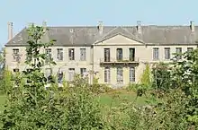 Vue d'un grand bâtiment abandonné avec des hautes herbes au premier plan