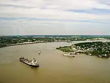 un large fleuve ocre, quelques gros bateaux. Sur les rives se déploie une ville verdoyante.