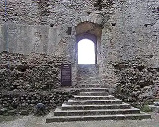 Photographie en couleurs d'une ouverture dans un mur à laquelle un escalier donne accès.