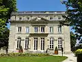 Bâtiment ancien en pierre blanche, de trois étages, avec un fronton triangulaire et un toit-terrasse.