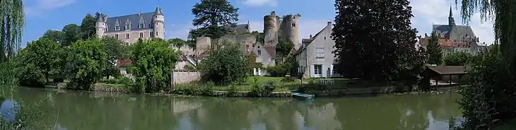 Photographie en couleurs d'un château Renaissance, de tours médiévales et d'une église du XVe siècle en arrière-plan d'un village au bord de l'eau.