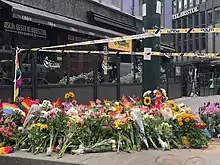 des bouquets de fleurs sur un trottoir, dont certains portent des drapeaux arc-en-ciel