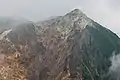 Photo couleur d'une montagne à la face avant érodée, sous un ciel nuageux.