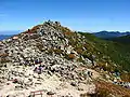 Photo couleur du sommet d'une montagne au sol parsemé de rochers gris, sous un ciel bleu.