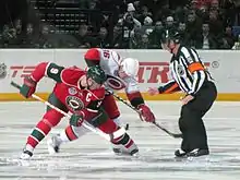 Photographie d'un arbitre effectuant une mise en jeu entre deux joueurs