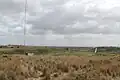 Antenne basse fréquence et son bâtiment de soutien au premier plan à gauche, champ d'antenne à haute fréquence en arrière-plan, bâtiment principal à droite.