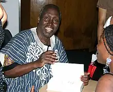 A smiling man faces the camera while opening a book