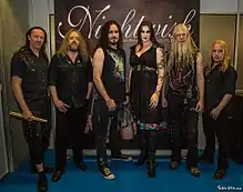Six membres d'un groupe de rock, cinq hommes et une femme, devant un drapeau publicitaire