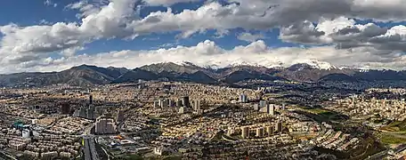 Devant de belles montagnes enneigées une grande ville, composée de quelques immeubles de grande hauteur, énormément de bâtiments, certains relativement bien rangés, d'autres s'accumulant sans ordre apparent, et quelques axes de circulation qui les traversent.
