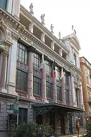 Vue d'un bâtiment de style italien du XVIIIe siècle à colonnes et grandes baies vitrées et statues sur son toit plat.
