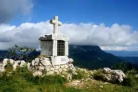 Petit monument en pierre, de forme cubique avec une niche dont l'ouverture est protégée par une grille, le tout surmonté d'une croix.