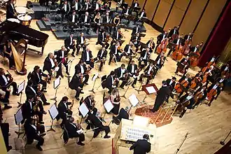 Orchestre philharmonique, plusieurs personnes habillées de noir, assises, tenant un instrument.