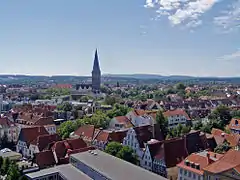 Photographie panoramique d'une ville : des toits rouges et le clocher d'une église domine.